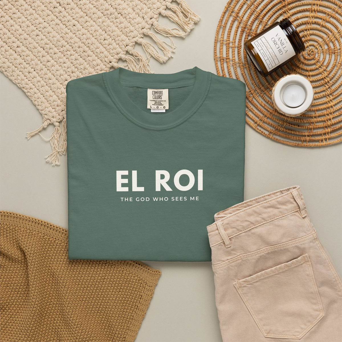 Blue spruce green El Roi Christian T-shirt with “The God Who Sees Me” typography, styled in a neutral flat lay.