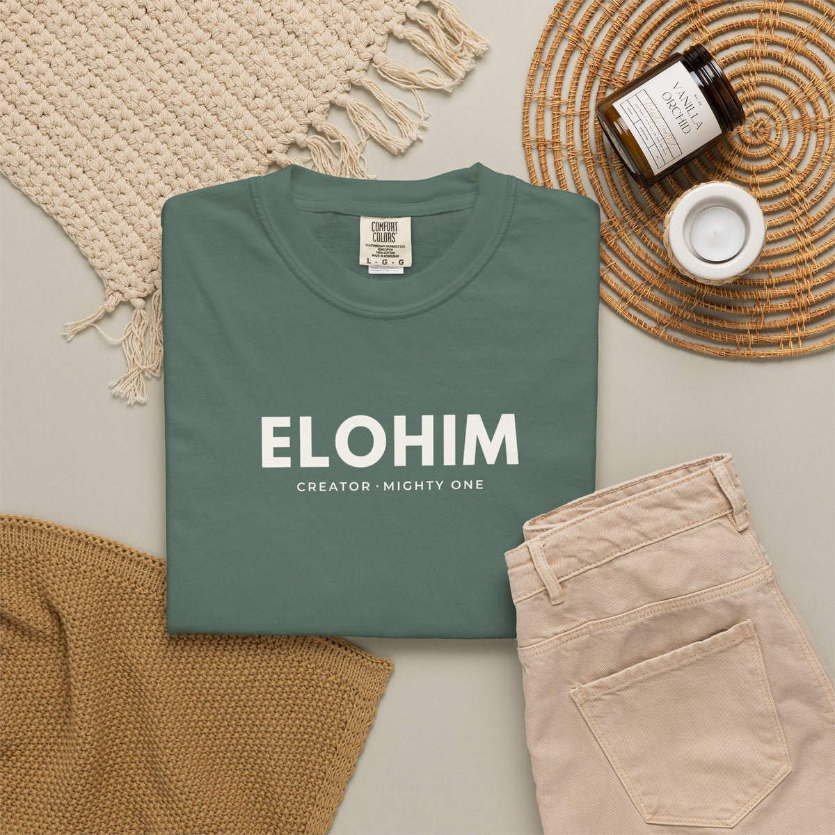 Blue spruce Elohim Christian T-shirt with “Creator · Mighty One” typography, styled in a neutral flat lay.