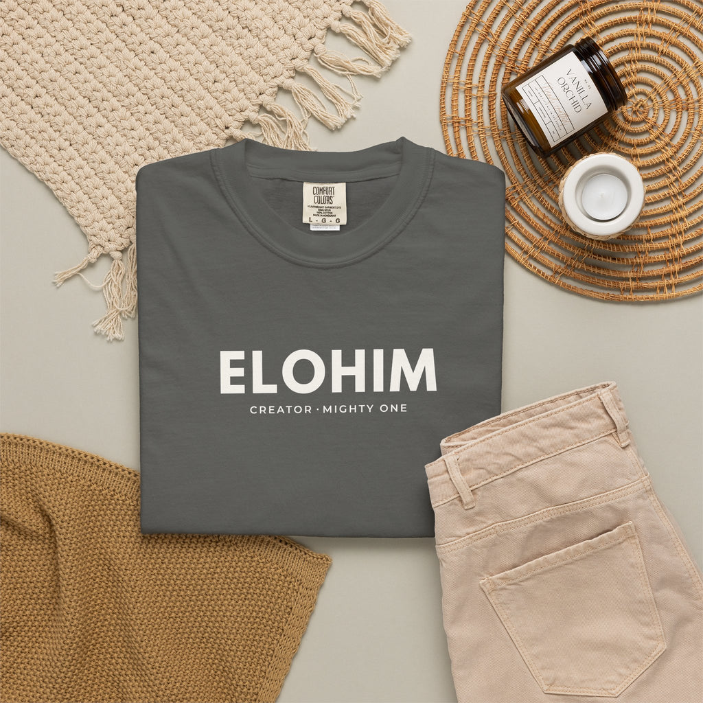 Pepper grey Elohim Christian T-shirt with “Creator · Mighty One” typography, styled in a neutral flat lay.