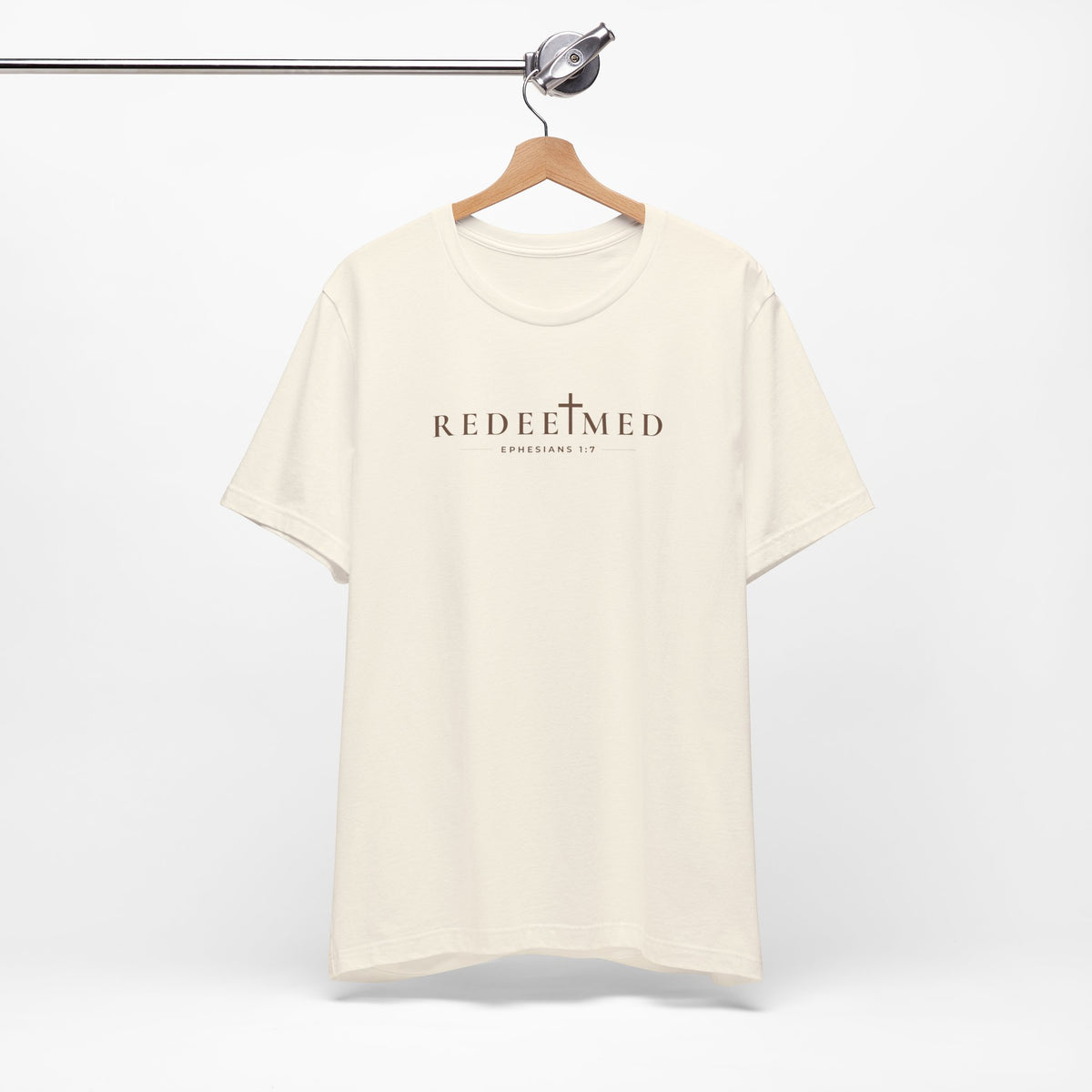 Natural Redeemed Christian T-shirt with cross detail and Ephesians 1:7 typography on hanger